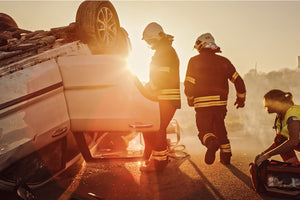 Stock photo of a wrecked vehicle upside down near sunset with first responders attempting to aid the victim.